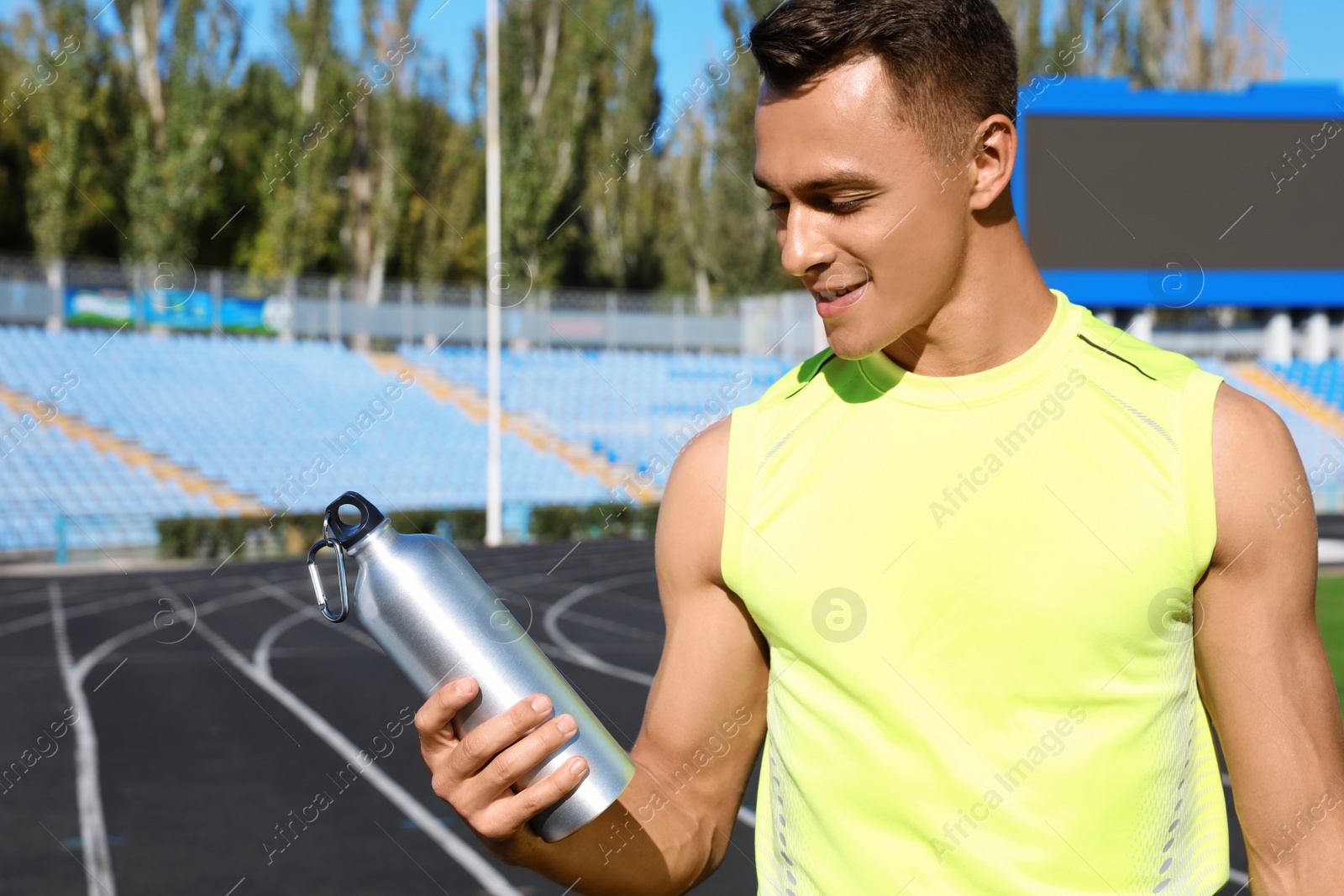 Photo of Sporty man with bottle of water at stadium on sunny day