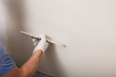 Worker plastering wall with putty knife indoors, closeup. Space for text