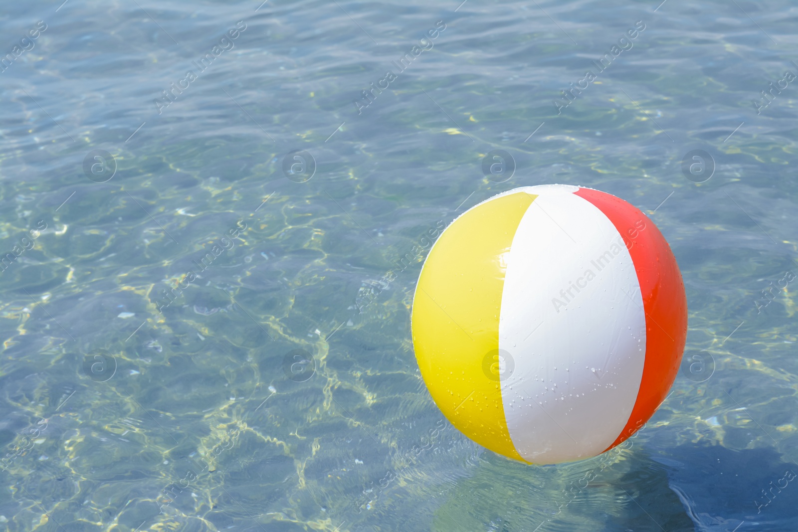 Photo of Colorful beach ball floating in sea on sunny day, space for text