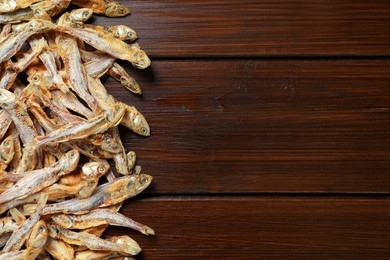 Photo of Tasty dried anchovies on wooden table, flat lay. Space for text