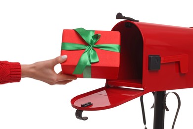 Woman putting Christmas gift into mailbox on white background, closeup. Sending present by mail