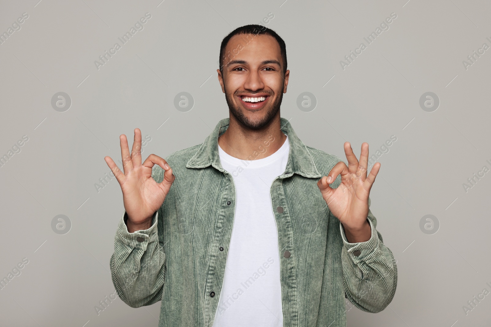 Photo of Smiling African American man showing ok gesture on light grey background