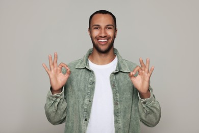 Smiling African American man showing ok gesture on light grey background