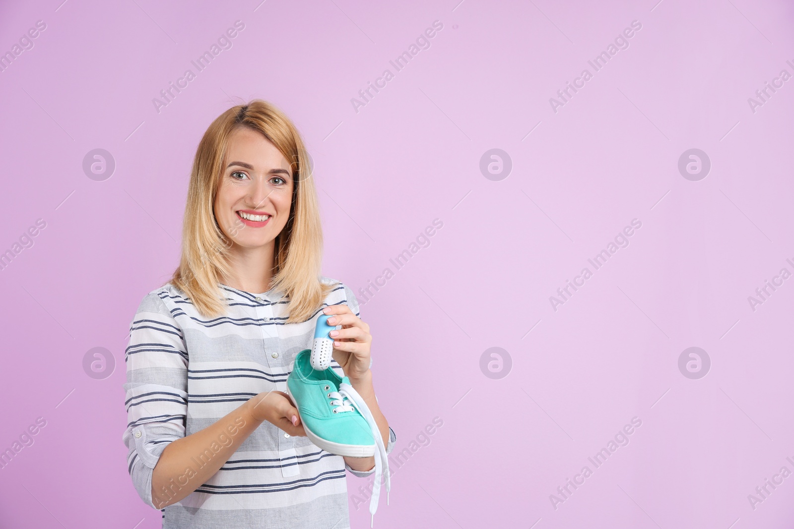 Photo of Young woman putting capsule air freshener in shoe on color background