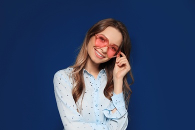 Photo of Portrait of beautiful young woman with heart shaped sunglasses on color background