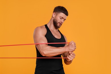 Photo of Young man exercising with elastic resistance band on orange background
