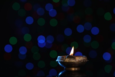 Photo of Lit diya on dark background with blurred lights, space for text. Diwali lamp