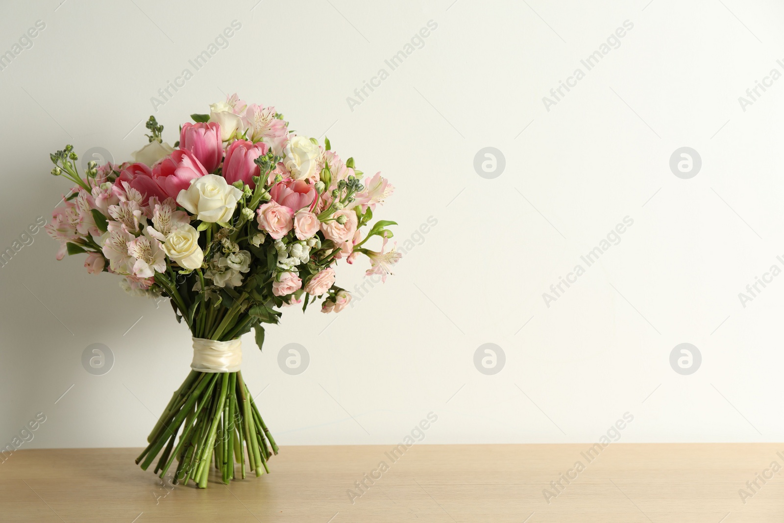 Photo of Beautiful bouquet of fresh flowers on wooden table near light wall. Space for text