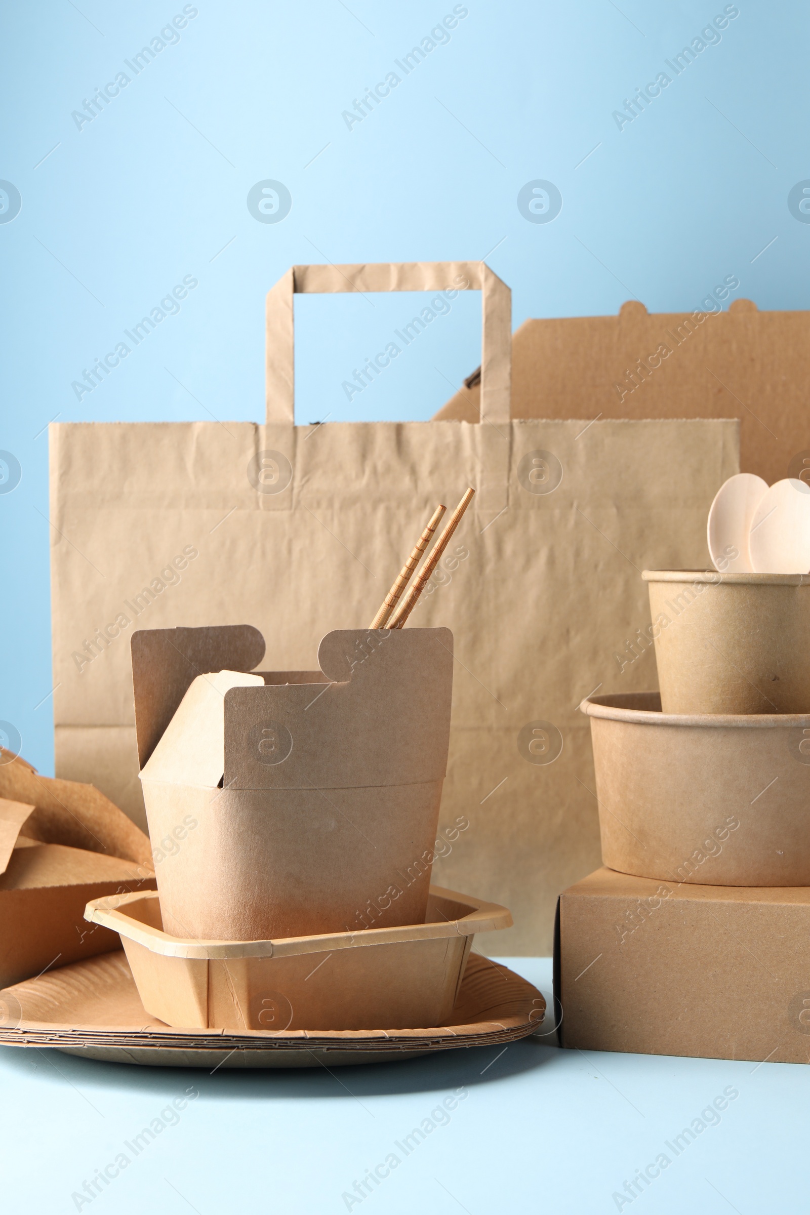 Photo of Eco friendly food packaging. Paper containers, tableware and bag on white table against light blue background