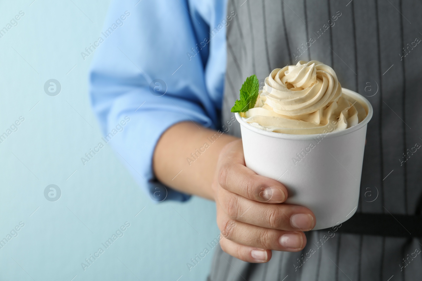 Photo of Woman holding cup with tasty frozen yogurt on blue background, closeup