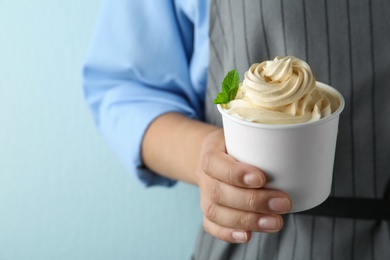 Photo of Woman holding cup with tasty frozen yogurt on blue background, closeup