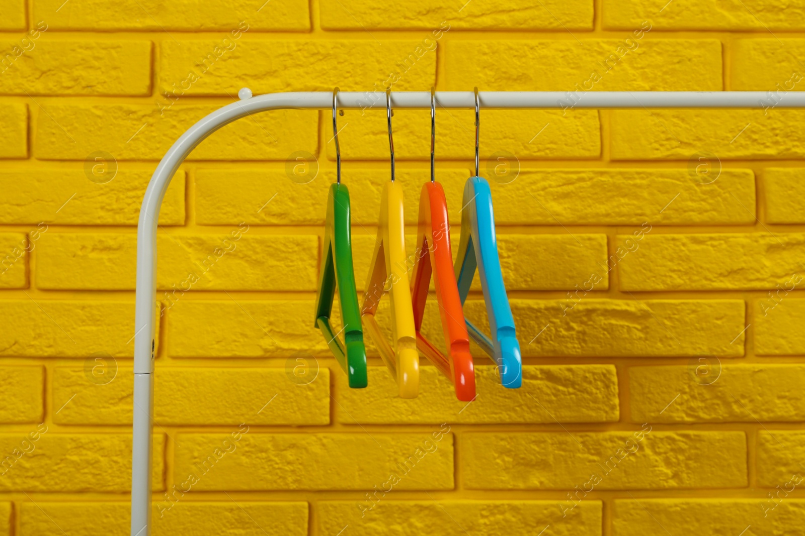 Photo of Wardrobe rack with many hangers near yellow brick wall