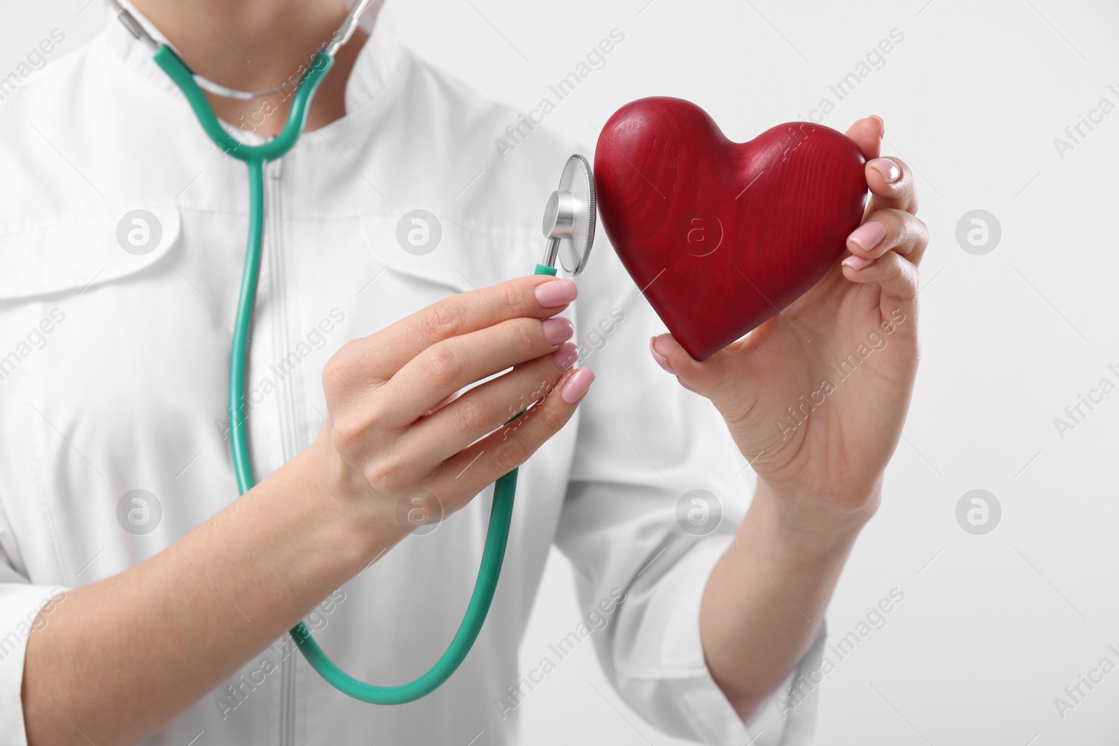 Photo of Doctor with stethoscope and red heart on white background, closeup. Cardiology concept