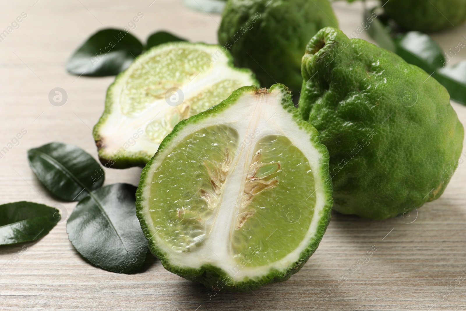 Photo of Whole and cut ripe bergamot fruits with green leaves on white wooden table, closeup