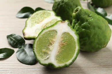 Photo of Whole and cut ripe bergamot fruits with green leaves on white wooden table, closeup