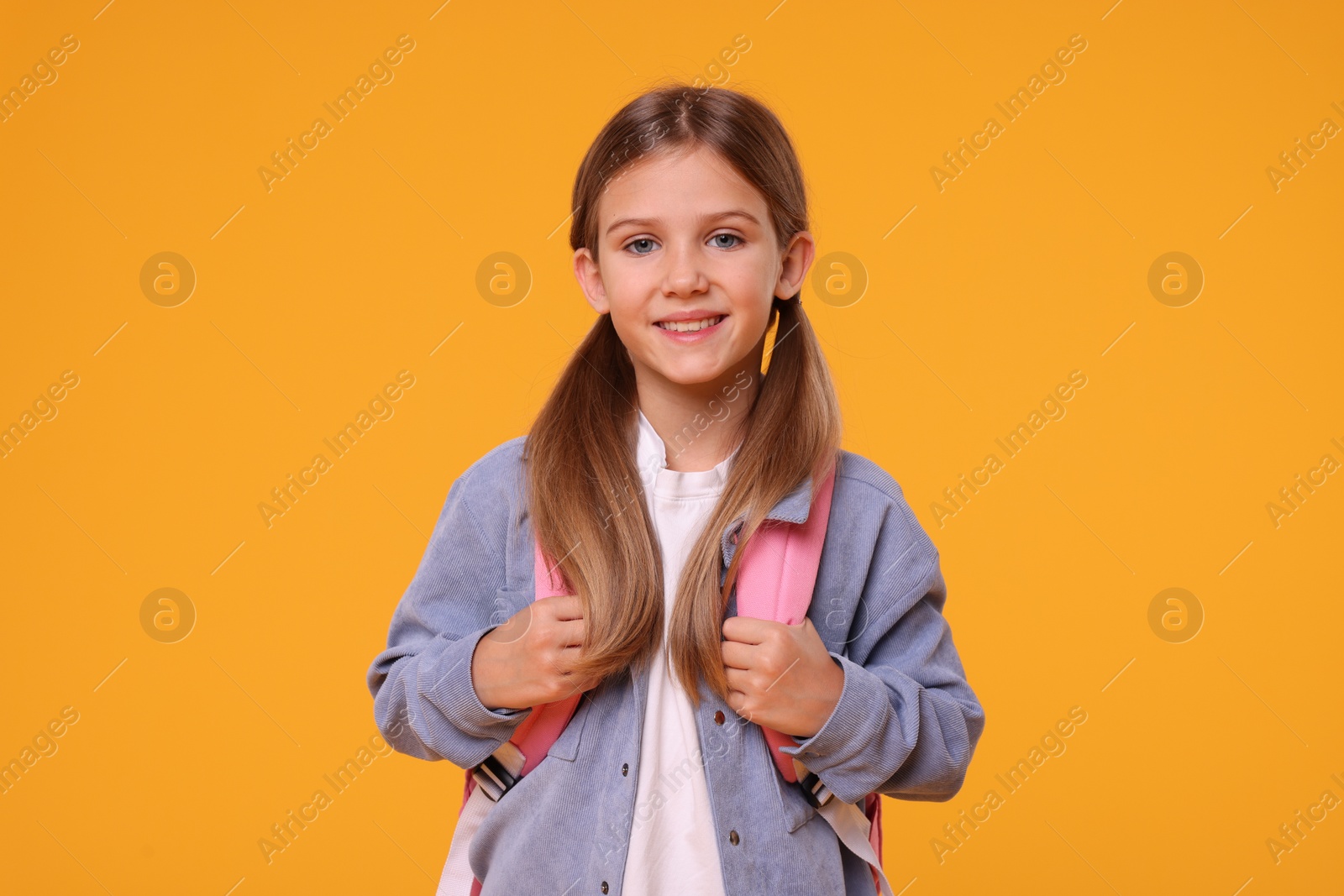 Photo of Happy schoolgirl with backpack on orange background