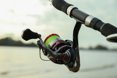 Photo of Fishing rod with reel near river, closeup