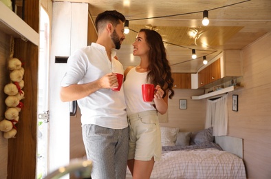 Photo of Happy young couple with cups in trailer. Camping vacation