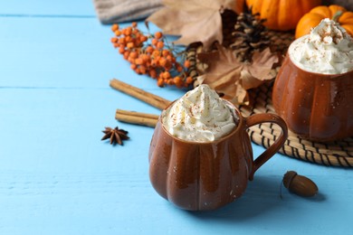 Photo of Mugs of pumpkin spice latte with whipped cream on light blue wooden table. Space for text