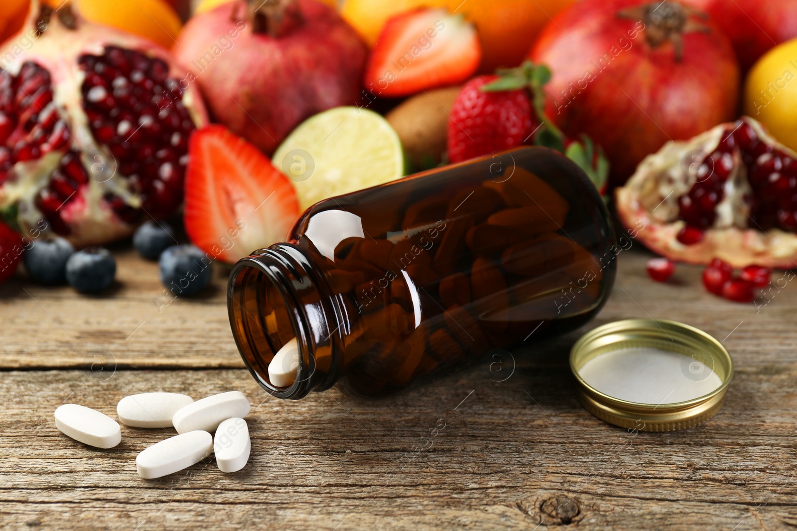 Photo of Vitamin pills, bottle and fresh fruits on wooden table