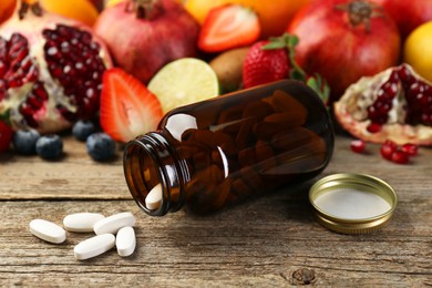 Photo of Vitamin pills, bottle and fresh fruits on wooden table