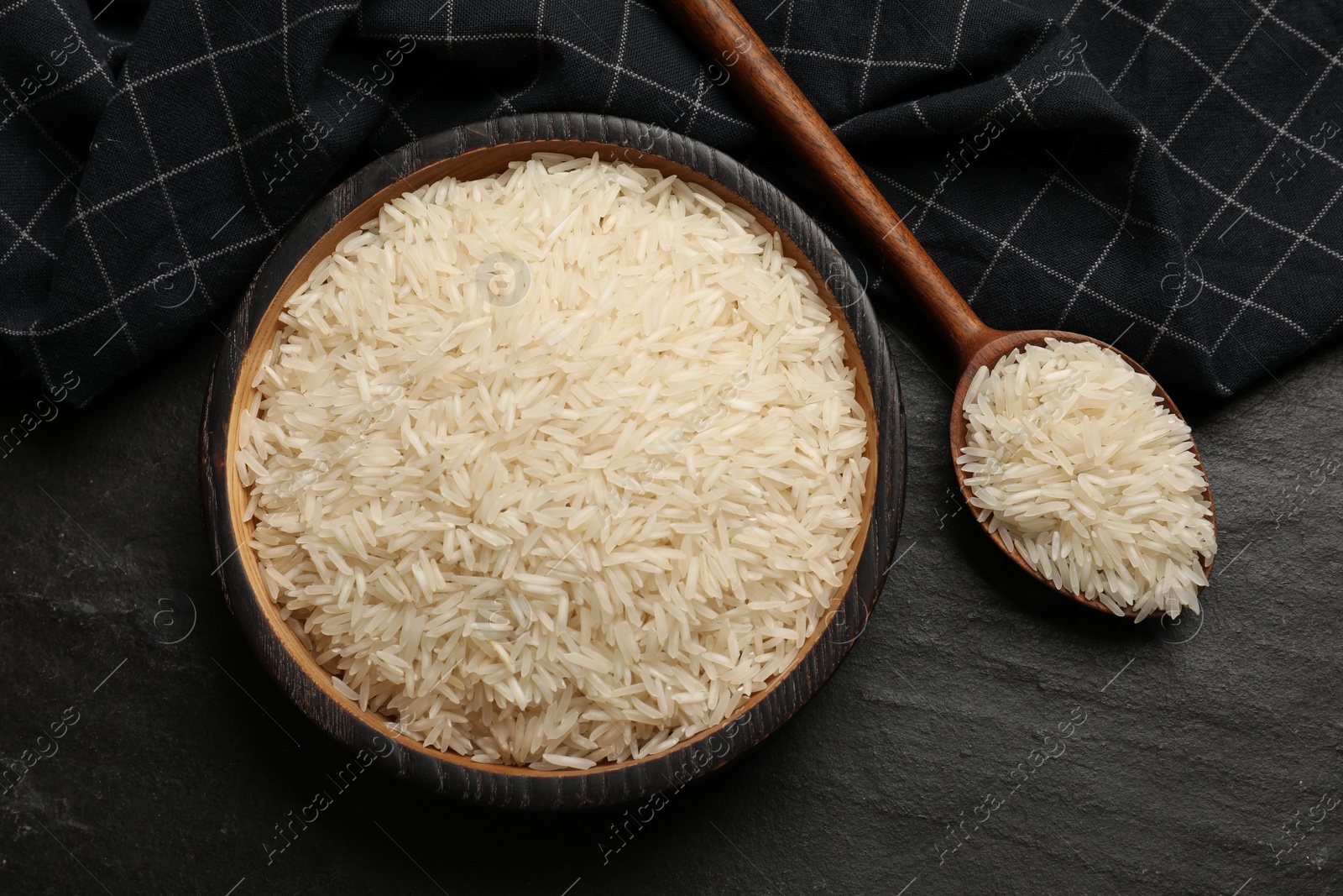 Photo of Raw basmati rice in bowl and spoon on black table, top view