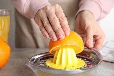 Photo of Woman squeezing orange juice at grey table, closeup