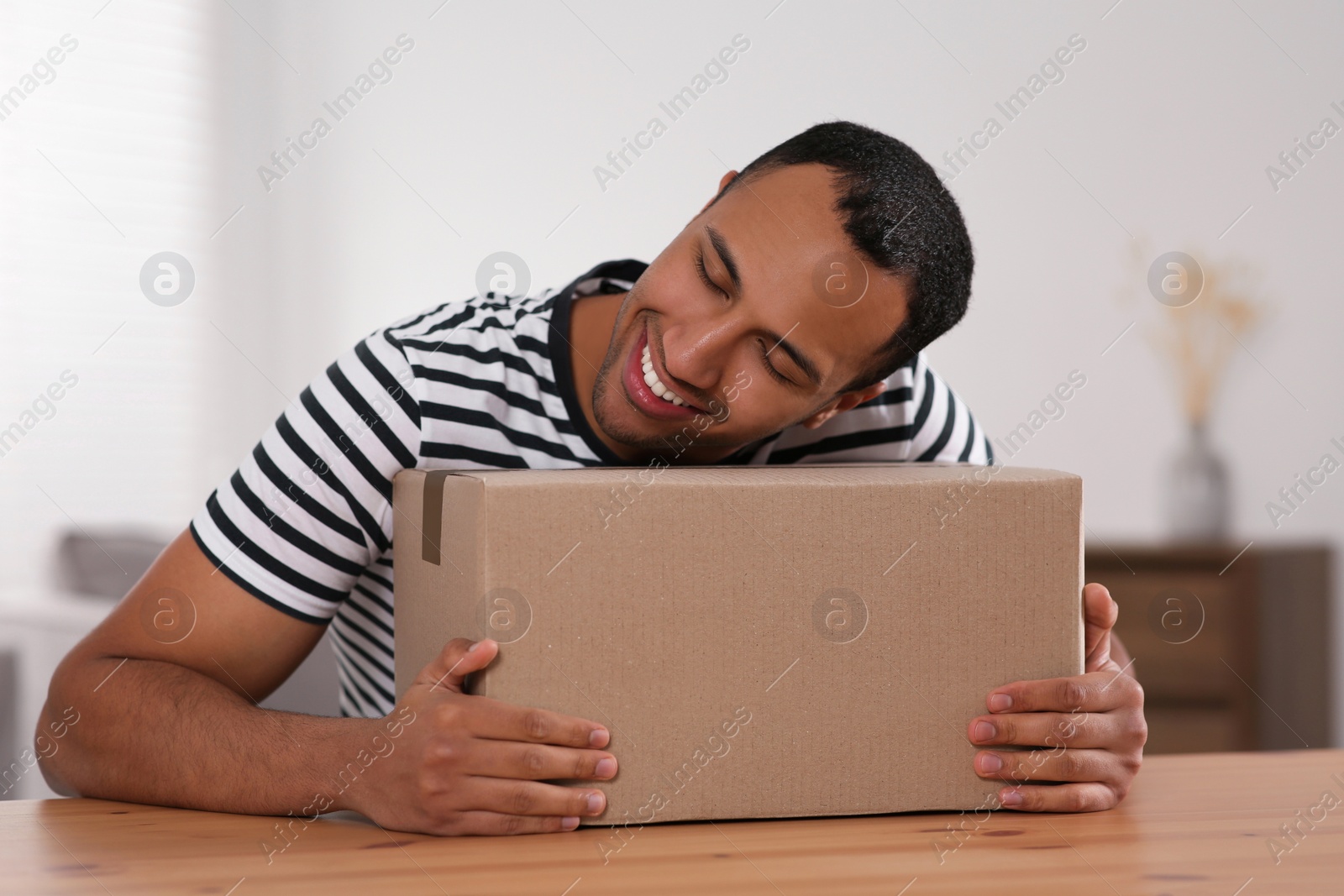 Photo of Happy young man with parcel at table indoors. Internet shopping