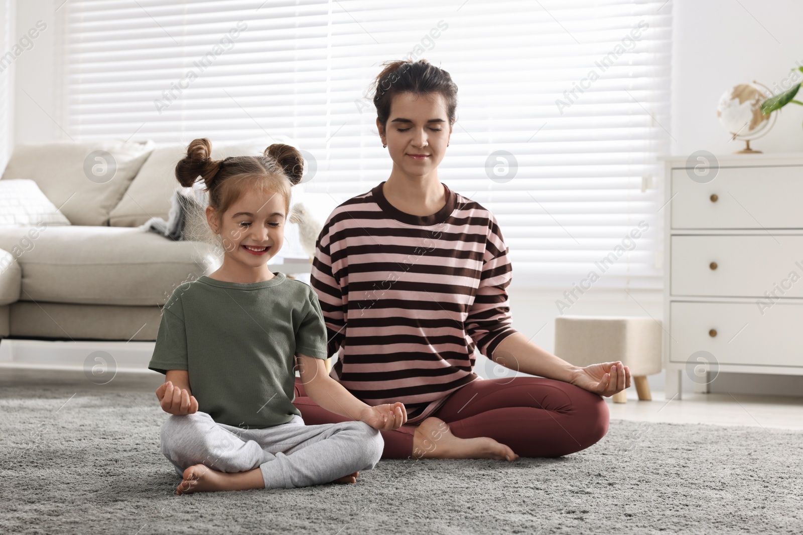 Photo of Young mother and her daughter meditating together at home