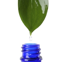 Photo of Essential oil drop falling from green leaf into glass bottle on white background, closeup