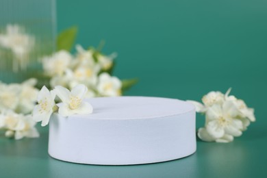 Presentation of product. White podium and beautiful jasmine flowers on green background, closeup