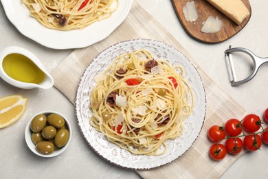 Delicious pasta with anchovies, tomatoes and parmesan cheese on light grey table, flat lay