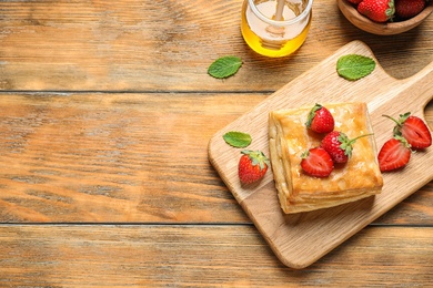 Photo of Fresh delicious puff pastry with sweet strawberries on wooden table, flat lay. Space for text
