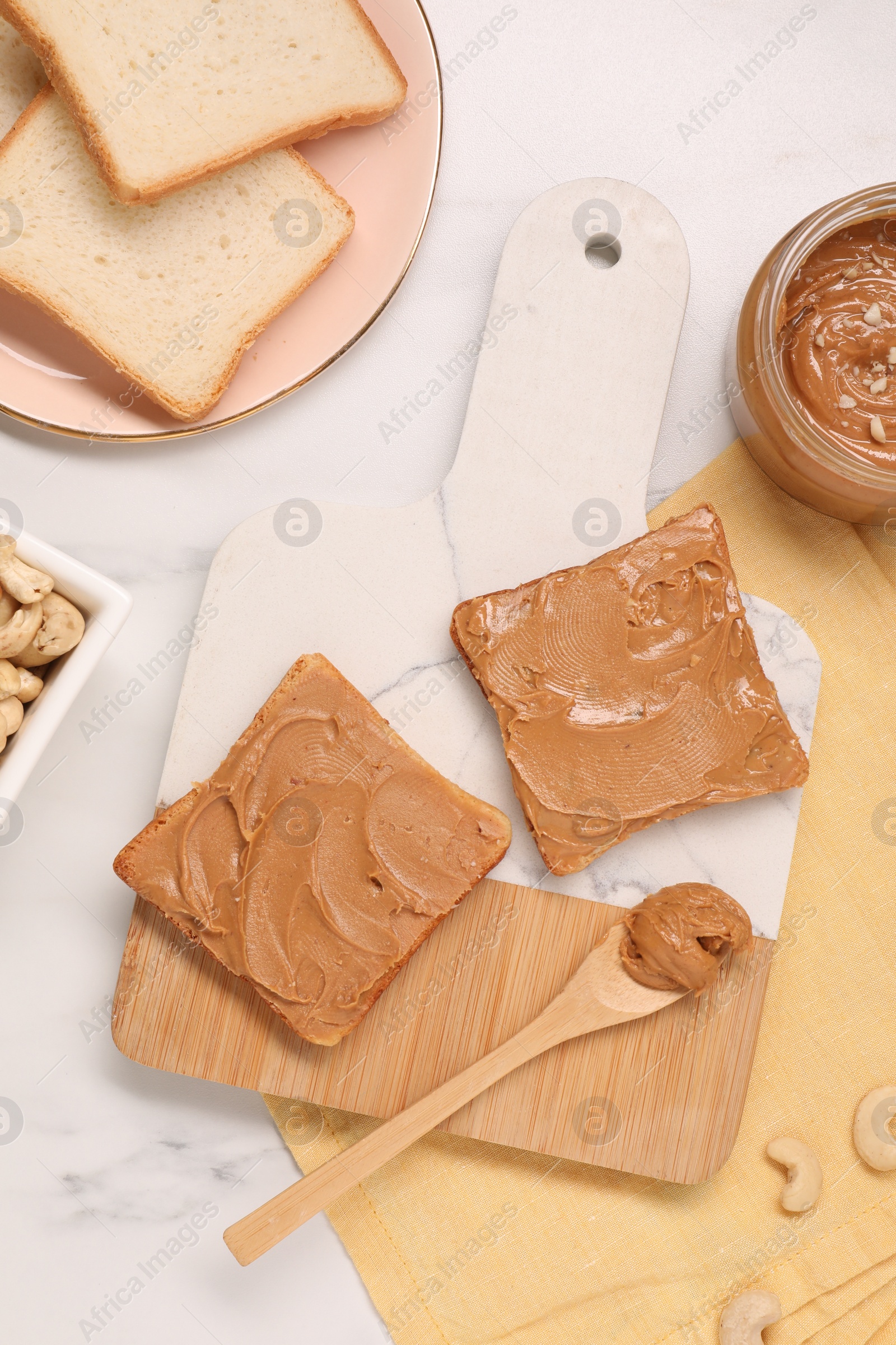 Photo of Toasts with tasty nut butter and cashews on white marble table, flat lay