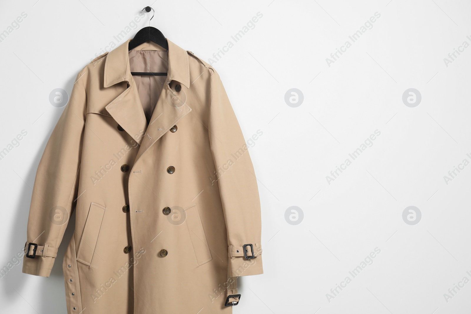 Photo of Hanger with beige trench coat on white wall, space for text