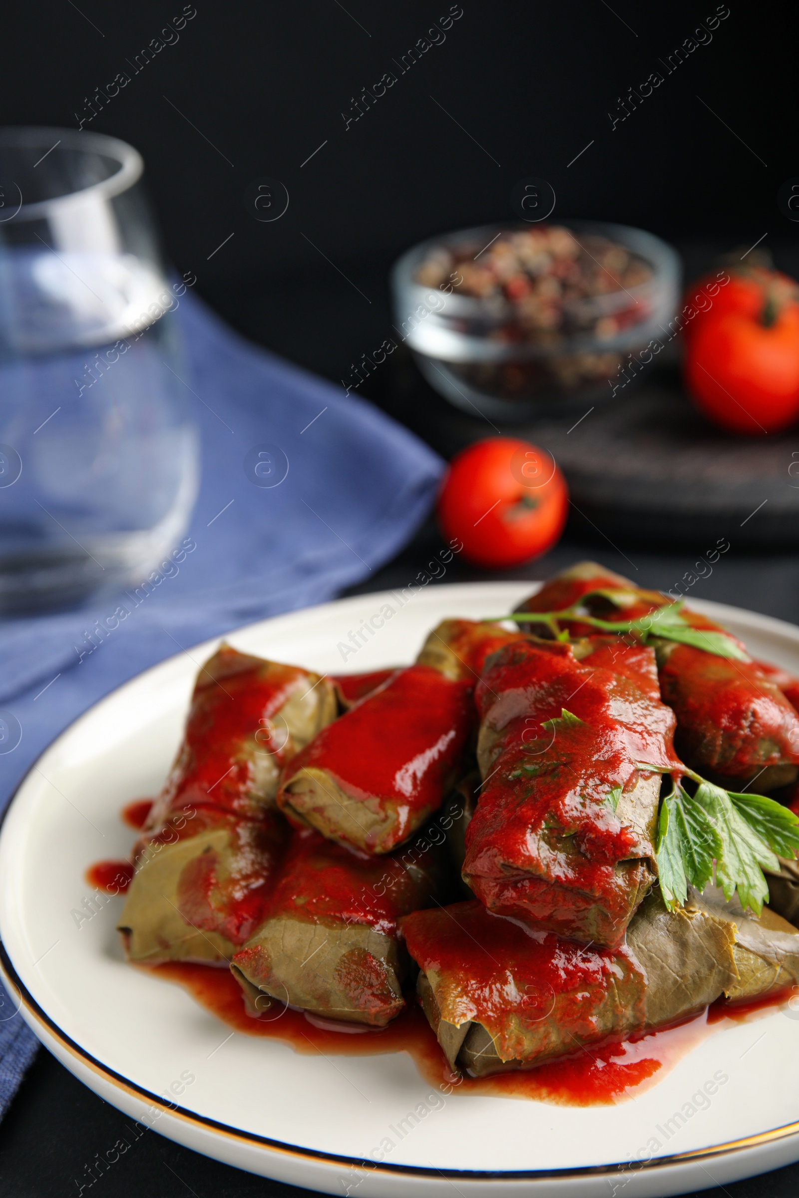 Photo of Delicious stuffed grape leaves with tomato sauce on table