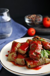 Delicious stuffed grape leaves with tomato sauce on table