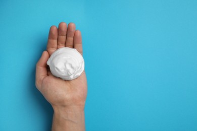 Man holding shaving foam on light blue background, top view. Space for text