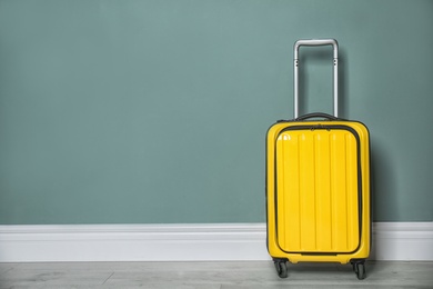 Bright yellow suitcase near color wall indoors