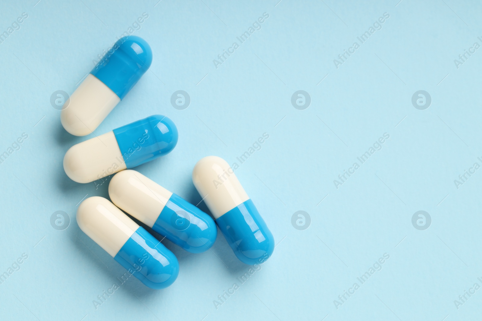 Photo of Many antibiotic pills on light blue background, top view. Space for text