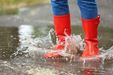 Woman with red rubber boots in puddle, closeup. Rainy weather