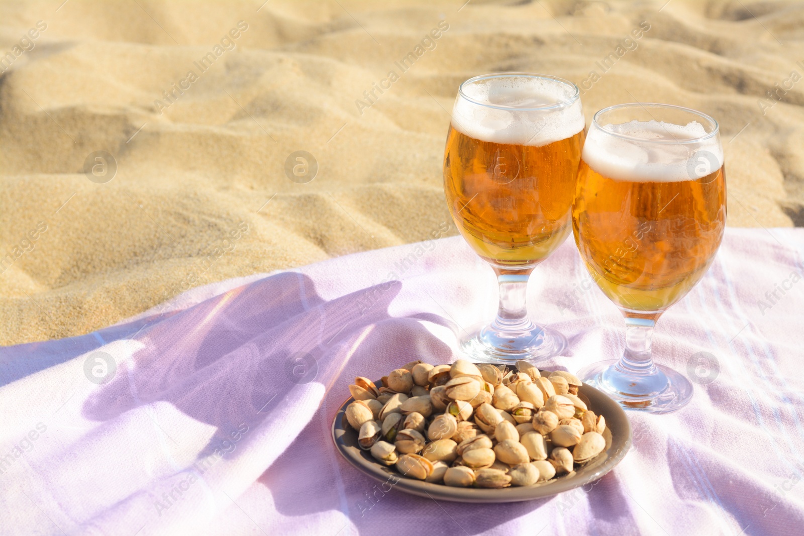 Photo of Glasses of cold beer and pistachios on sandy beach, space for text