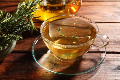 Photo of Cup of aromatic herbal tea, fresh rosemary and thyme on wooden table