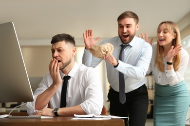 Photo of Coworkers popping paper bag behind their colleague in office. Funny joke