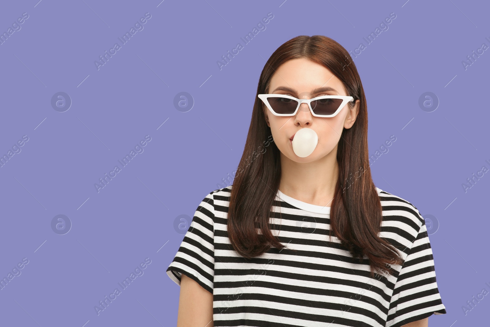 Photo of Beautiful woman in sunglasses blowing bubble gum on light purple background, space for text