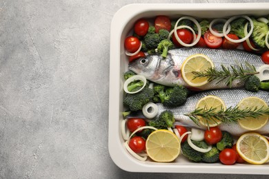 Photo of Raw fish with vegetables and lemon in baking dish on grey textured table, top view. Space for text