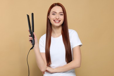Beautiful woman with hair iron on beige background