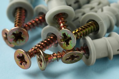 Many metal screws with dowels on light blue background, closeup