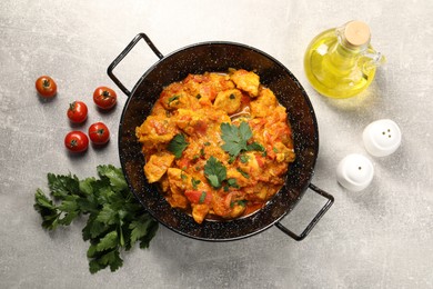 Photo of Delicious chicken curry in frying pan, parsley, tomatoes and oil on light grey table, flat lay
