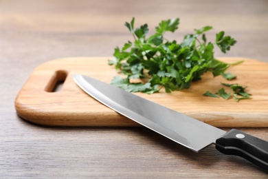 Photo of Cutting board with chef's knife and fresh parsley on wooden table